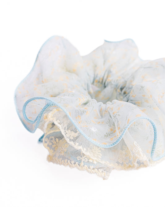 Close-up of light blue sheer floral hair scrunchie showing fabric texture and scalloped lace trim details