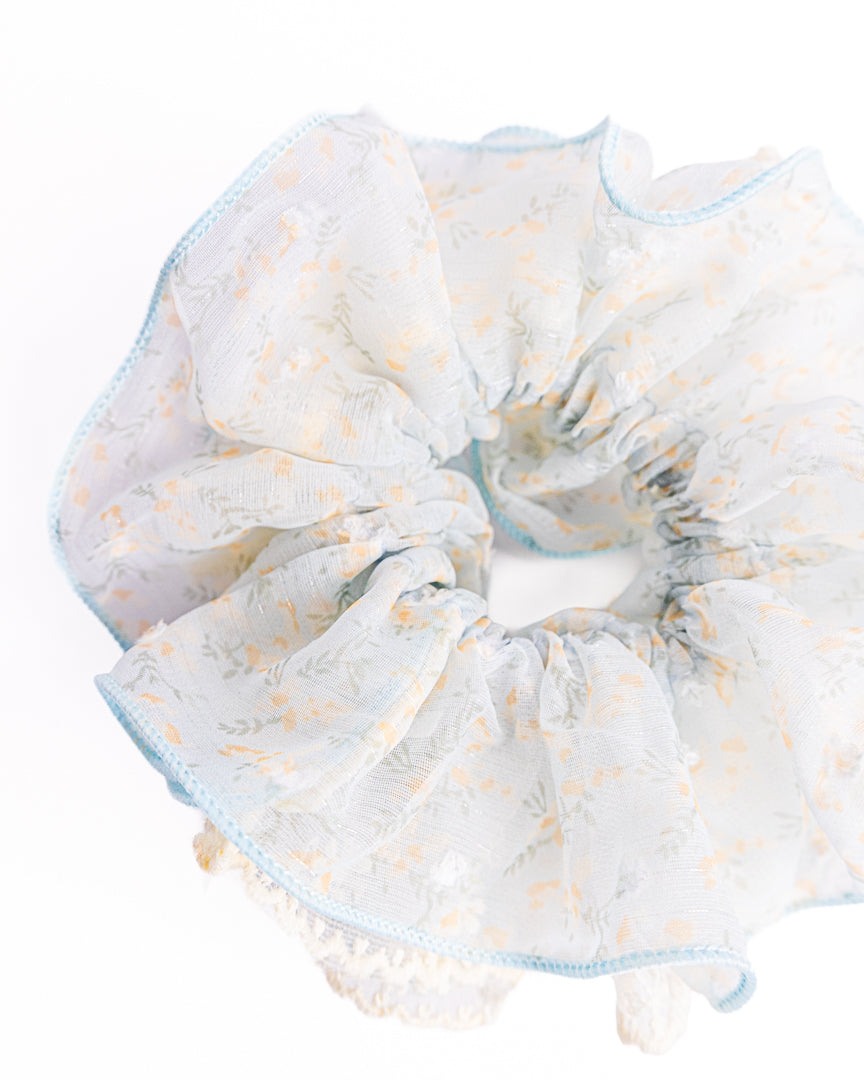 Side view of fluffy light blue sheer floral hair scrunchie with embroidered edge highlighting voluminous ruffles