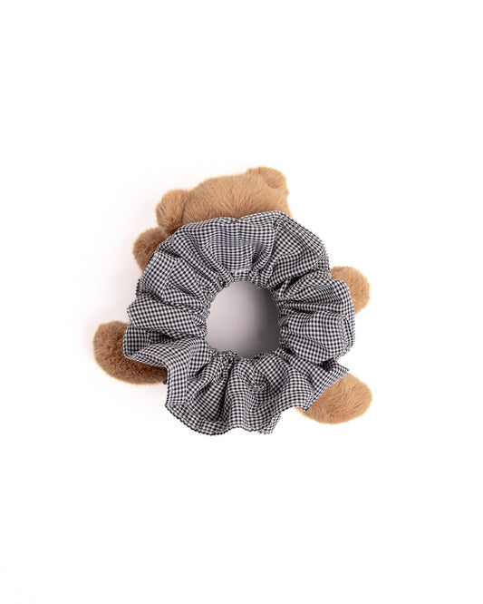 Close-up of brown teddy bear plush hair scrunchie showing soft toy face and black check gingham fabric ruffles