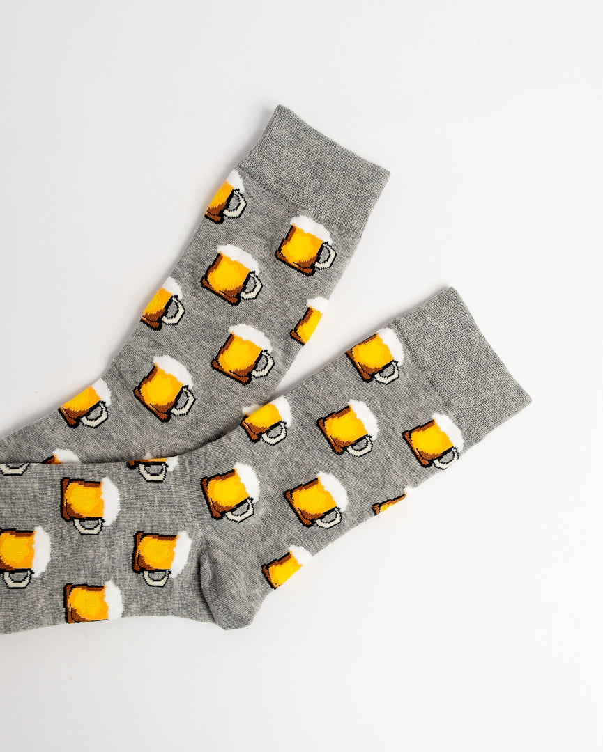 A pair of heather gray crew socks with a repeating pattern of yellow beer mugs with white foam, laid flat on a white background.