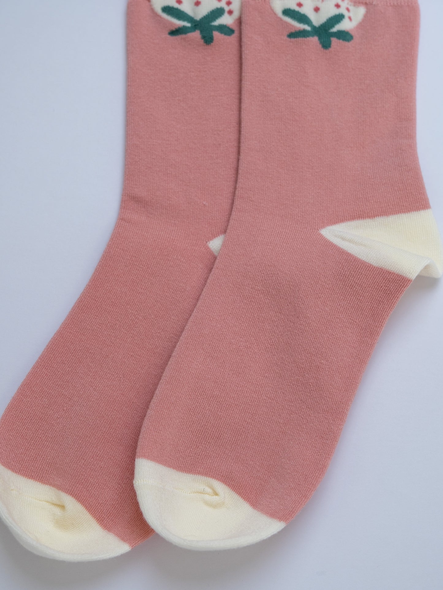 Pink socks with white toes and green floral patterns on a light gray background