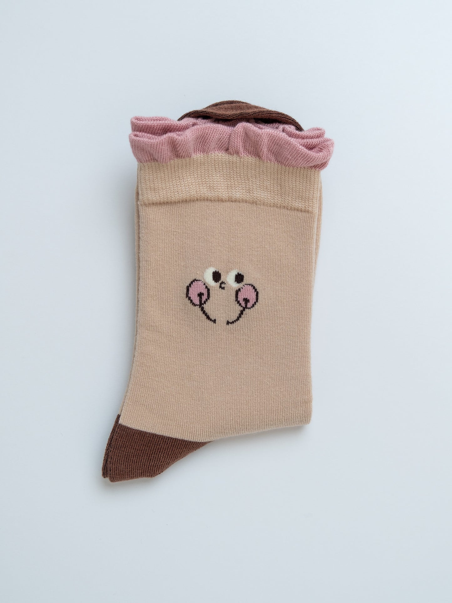 Beige sock with pink ruffled top and cartoon face design on a light gray background