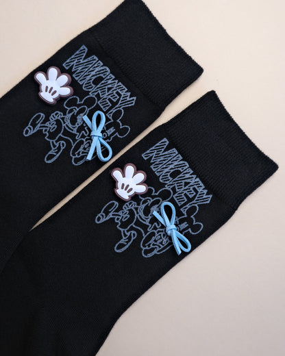 Black socks with embroidered designs of a cartoon character on a beige background