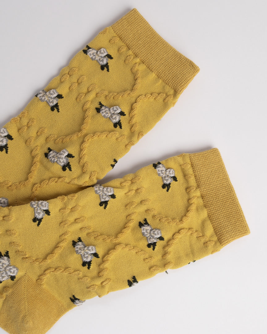 Mustard yellow knitted leg warmers with black and white floral patterns on a light gray background