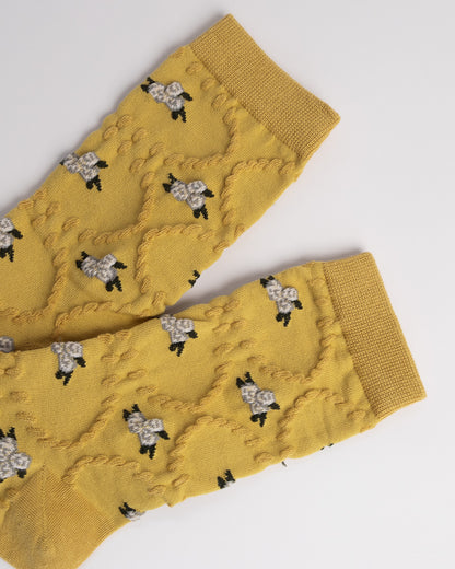 Mustard yellow knitted leg warmers with black and white floral patterns on a light gray background
