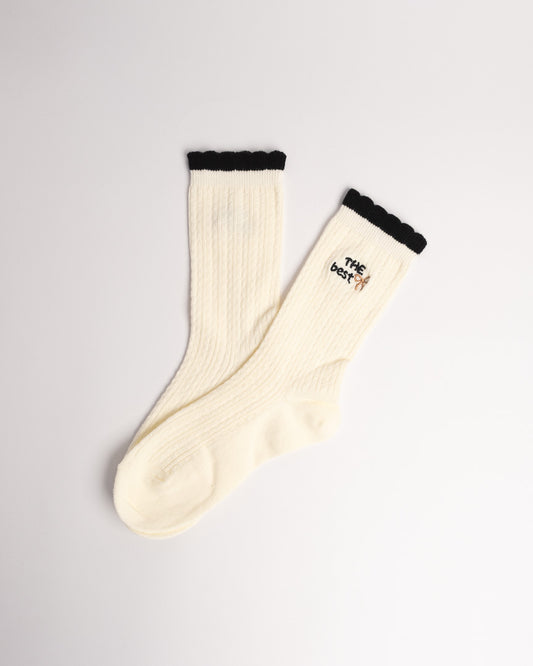 Close-up of cream ribbed cotton socks with embroidered bow detail and ruffle trim