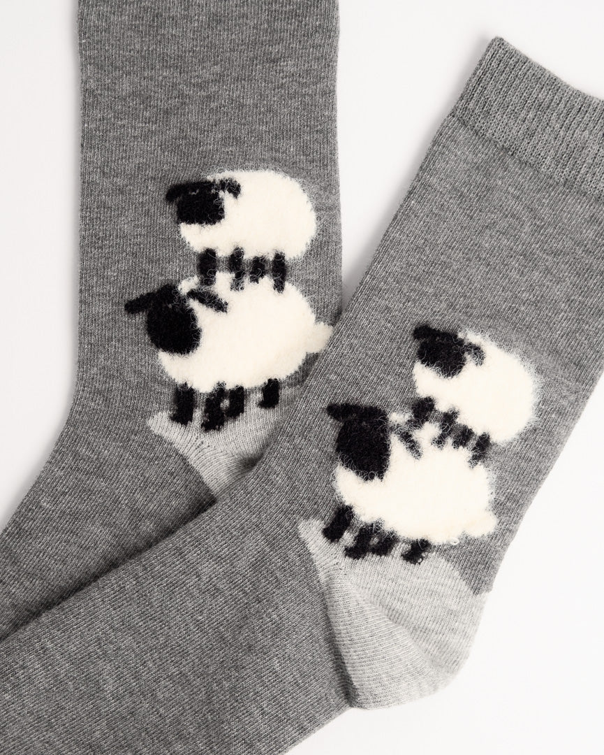 A pair of heather gray knit socks featuring a large white and black sheep motif on each sock, photographed against a plain white background.