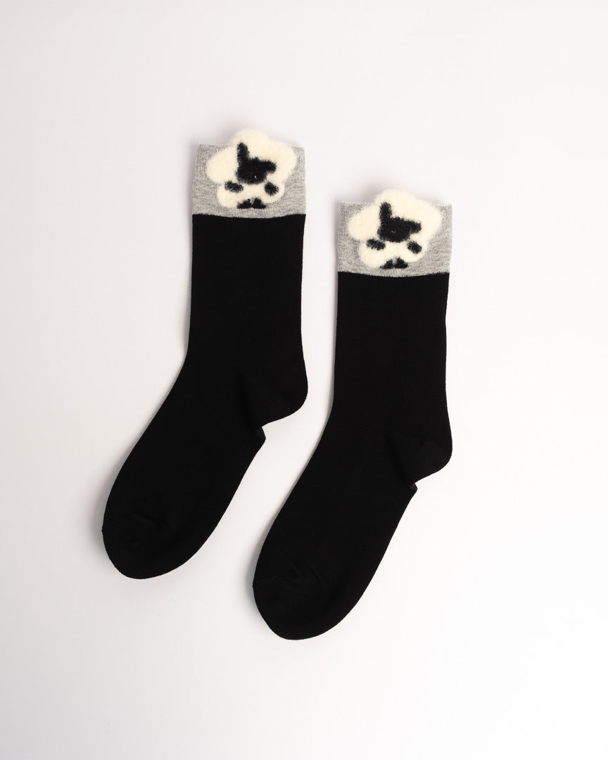 A pair of black crew socks with a gray ribbed cuff and a fluffy cream dog paw print detail, displayed on a clean white background.