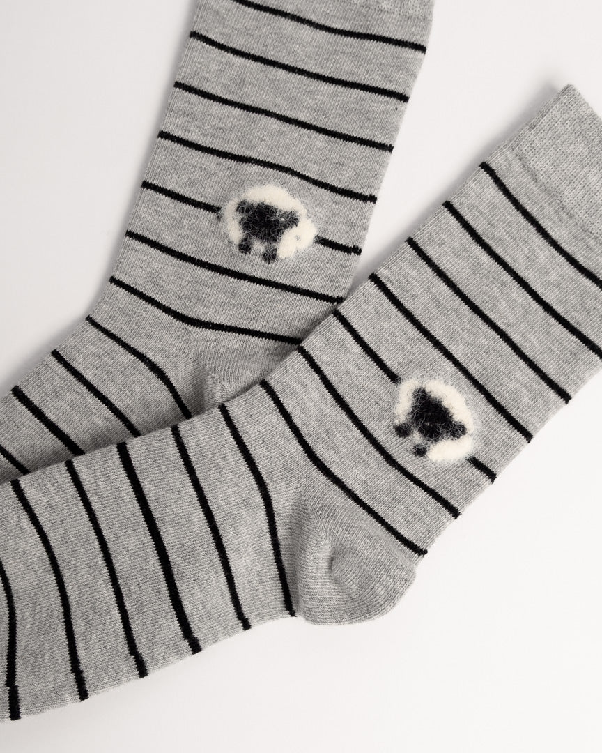A pair of gray knit socks with thin black horizontal stripes and a small fluffy black-and-white sheep motif near the lower calf, displayed on a clean white background.