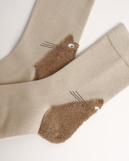 A pair of beige ribbed socks with brown fuzzy cat-shaped heels, shown on a plain light background.
