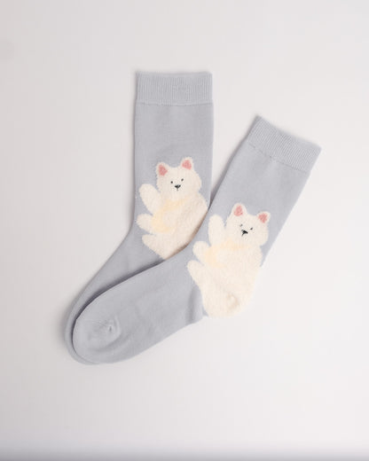 A pair of light blue crew socks with fluffy cream-colored cat graphics on the front, displayed on a clean white background.