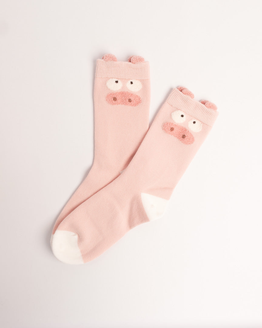 A pair of light pink baby socks with a cute pig face design on the cuff and white toes, displayed on a clean white background.