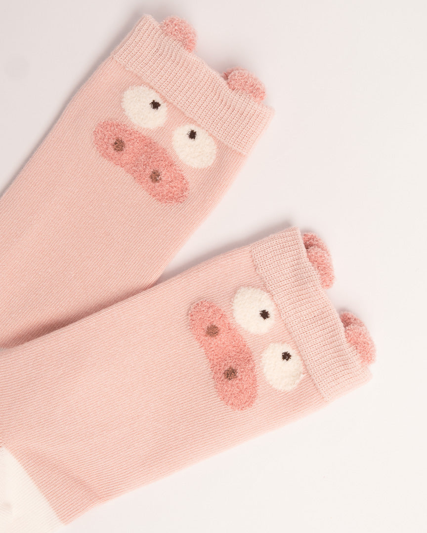A pair of light pink knit arm warmers featuring a cute pig face design with embroidered pink snout, white eyes, and small pink ears on the cuff, shown on a plain white background.