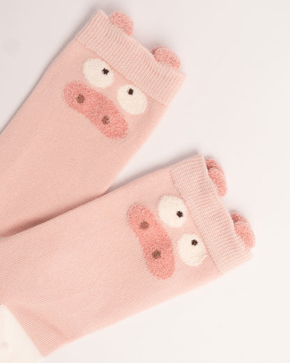 A pair of light pink knit arm warmers featuring a cute pig face design with embroidered pink snout, white eyes, and small pink ears on the cuff, shown on a plain white background.
