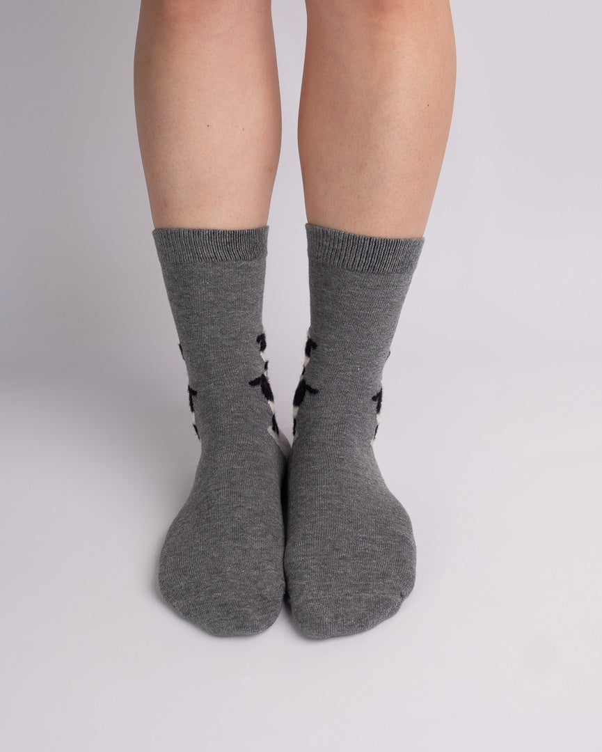 A pair of heather gray crew socks with black side patterns, worn on a person's legs against a light gray studio background.