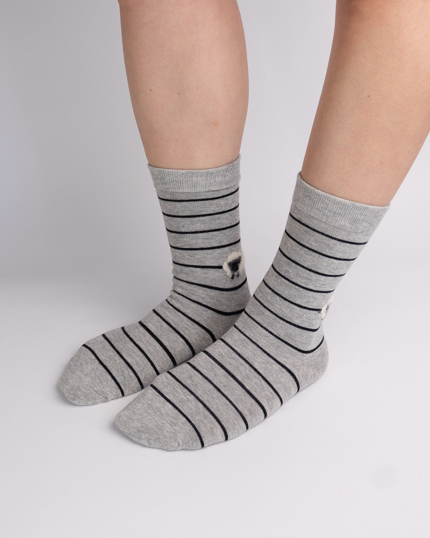 A pair of gray crew socks with thin black horizontal stripes and a small white graphic on the side, shown worn on a person's feet against a light gray studio background.