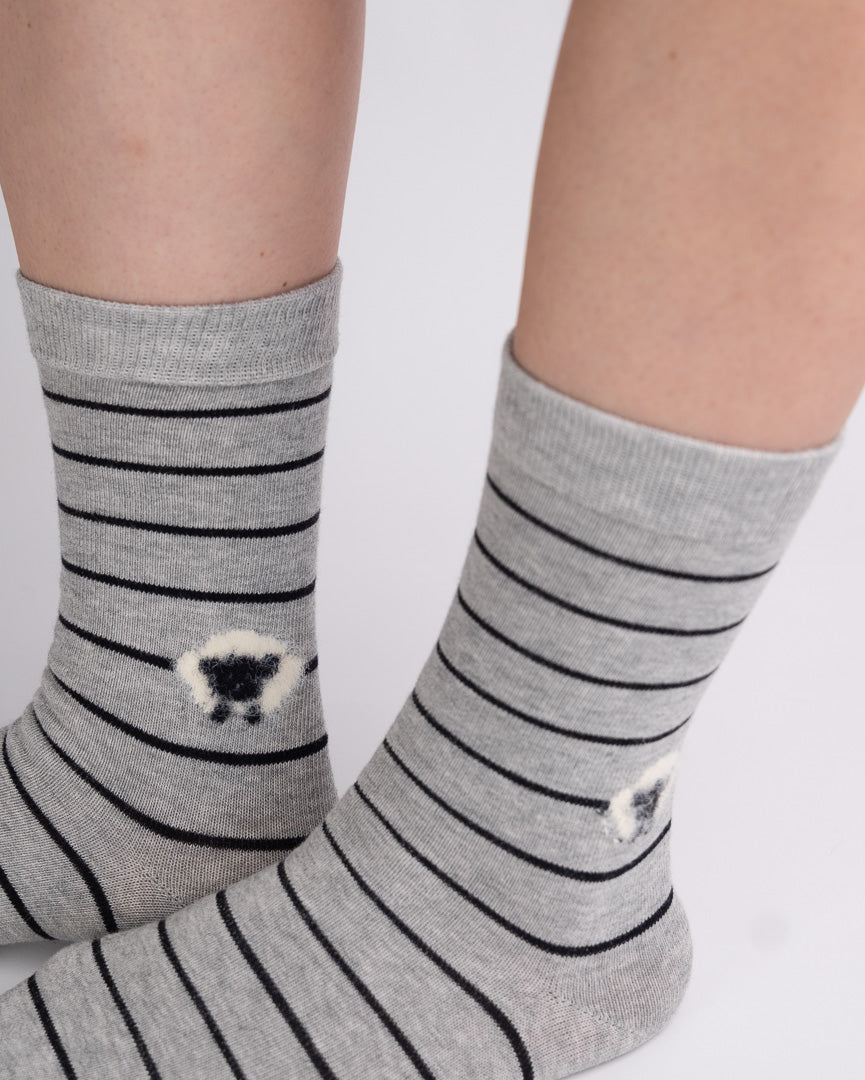 Gray crew socks with thin black horizontal stripes and small white sheep motifs near the cuffs, worn on feet against a plain light background.