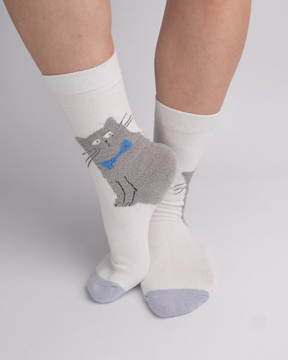 White crew socks worn on a person's feet, featuring a gray cat graphic with a blue bow tie on the front sock.