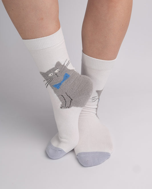 White crew socks worn on a person's feet, featuring a gray cat graphic with a blue bow tie on the front sock.
