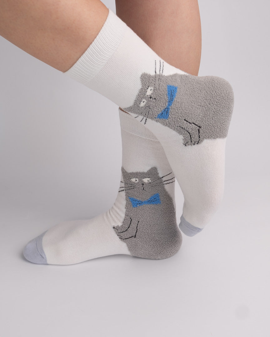White crew socks with gray cat graphics wearing them, shown on a person's legs against a light gray studio background.