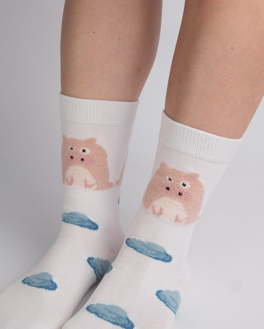 White crew socks with a pink cartoon hamster and blue cloud pattern, shown on a person's feet against a light gray background.