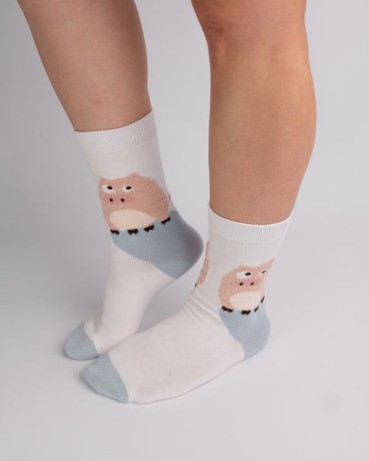 White crew socks with a cute cartoon owl design in pink and light blue, worn on a person's feet against a light gray studio background.