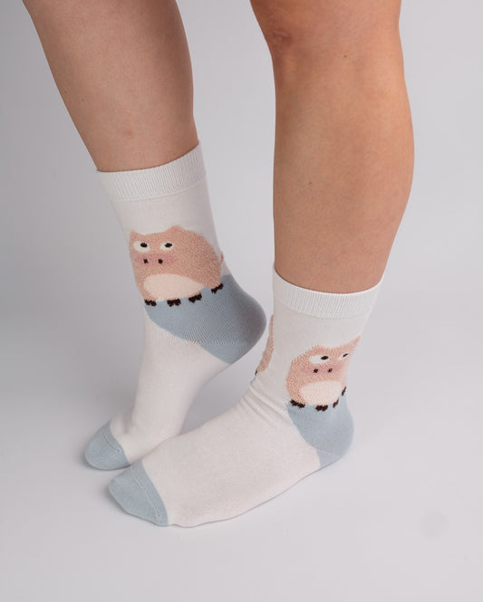 White crew socks with a cute cartoon owl design in pink and light blue, worn on a person's feet against a light gray studio background.