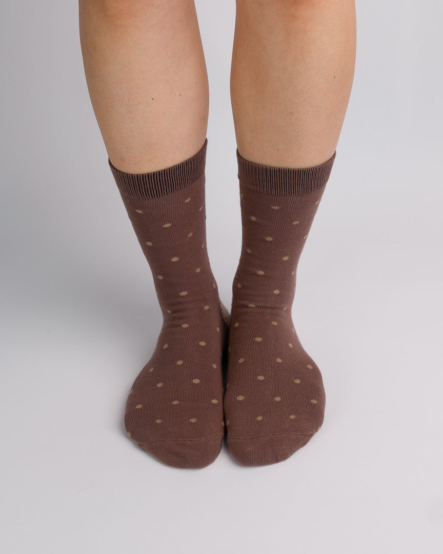 A pair of brown crew socks with small tan polka dots, worn on a person's legs against a light gray studio background.