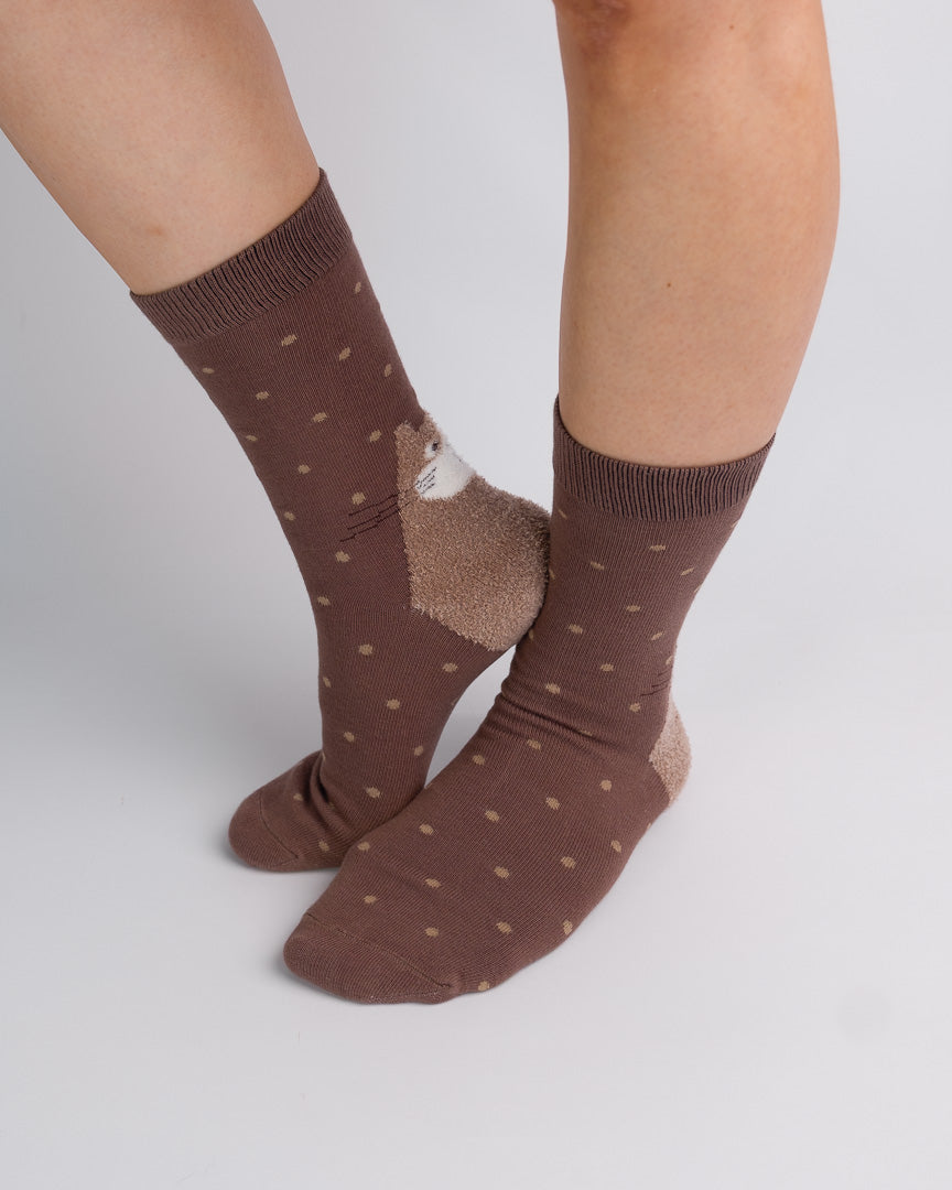 A pair of brown crew socks with small tan polka dots and a textured tan heel patch, shown on a person's feet against a light gray studio background.