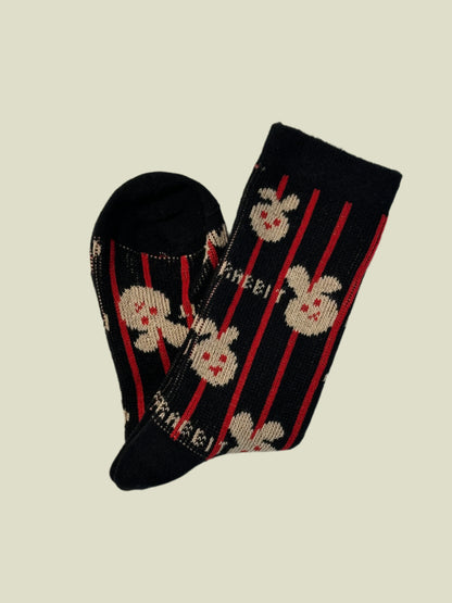 Black sock with red stripes and white floral patterns on a light gray background