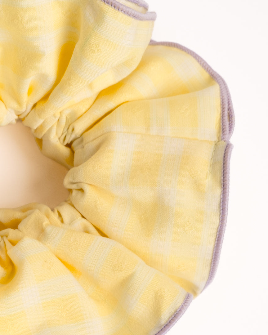 Close-up of yellow gingham cotton scrunchie showing fabric texture and purple edge trim details