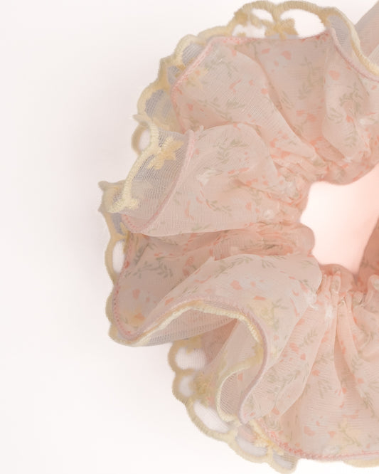 Close-up of pink sheer floral hair scrunchie showing fabric texture and yellow scalloped lace trim details