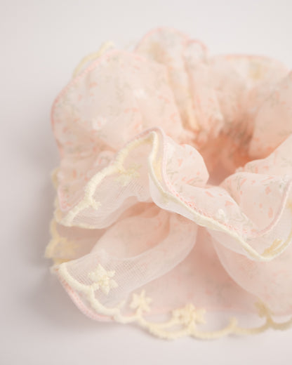 Side view of fluffy pink sheer floral hair scrunchie with yellow embroidered edge highlighting voluminous ruffles