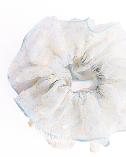 Side view of fluffy light blue sheer floral hair scrunchie with embroidered edge highlighting voluminous ruffles