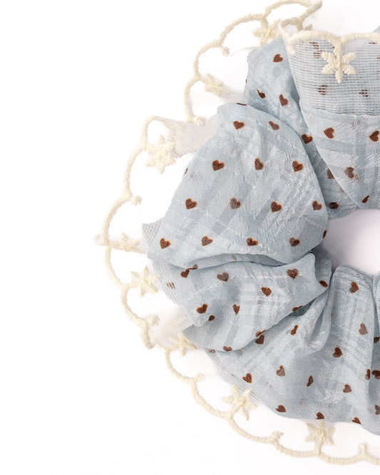 Side view of fluffy light blue sheer heart hair scrunchie with white embroidered lace trim highlighting voluminous ruffles