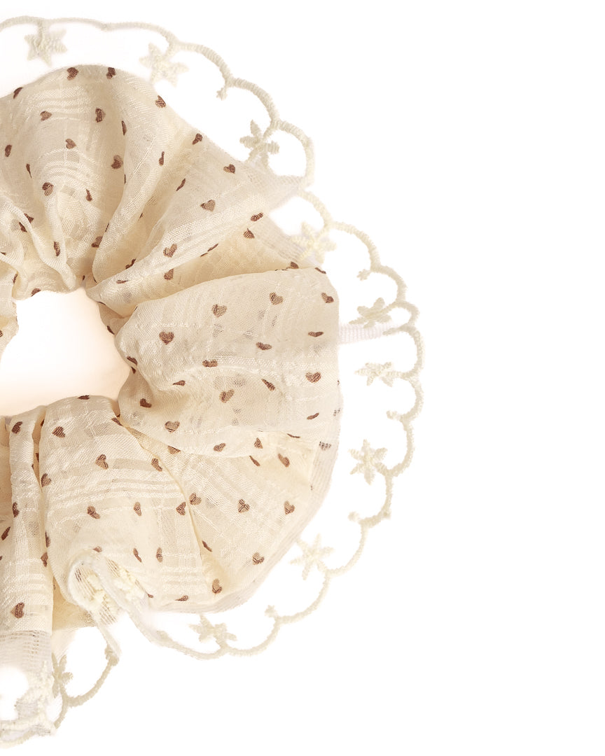 Close-up of cream sheer heart hair scrunchie showing fabric texture and scalloped lace trim details