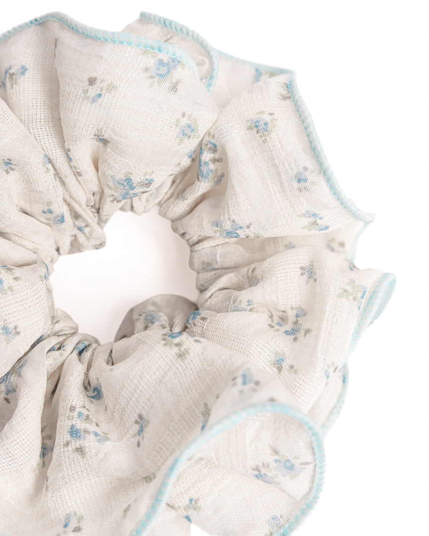 Close-up of cream sheer floral hair scrunchie showing fabric texture and blue trim details