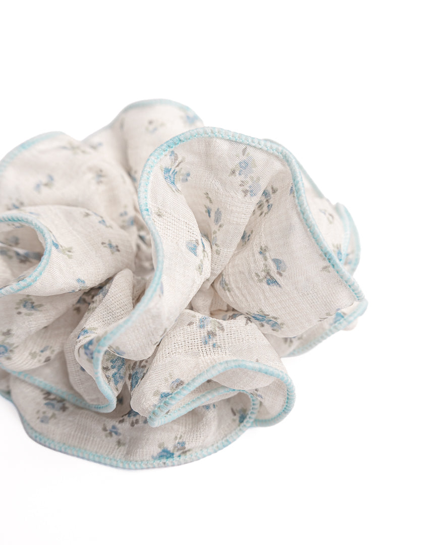 Side view of fluffy cream sheer floral hair scrunchie with blue trim highlighting voluminous ruffles