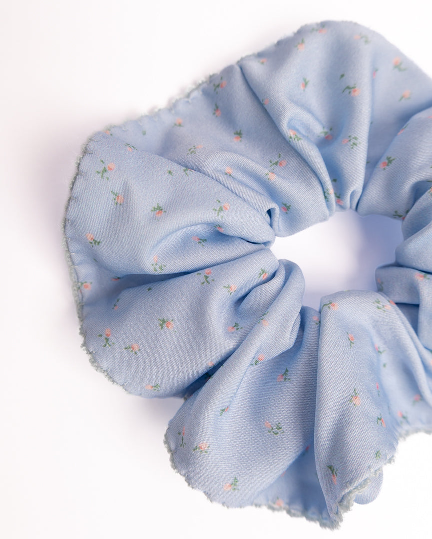 Close-up of light blue ditsy floral silky hair scrunchie showing smooth fabric texture and scalloped lace trim details