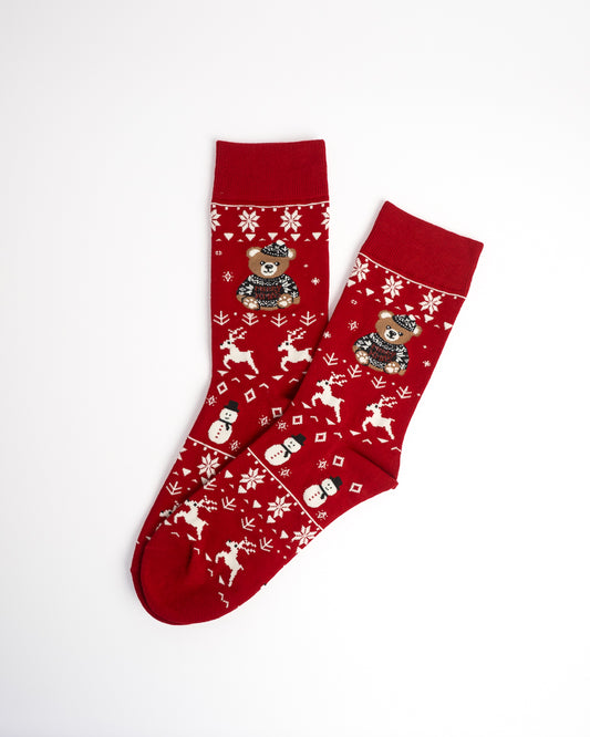 A pair of red Christmas crew socks with white snowflake and reindeer patterns, featuring a teddy bear wearing a Santa hat on the upper leg.