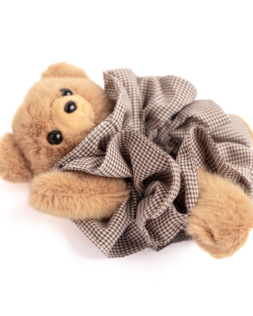 Close-up of brown teddy bear plush hair scrunchie showing soft toy face and gingham fabric ruffles