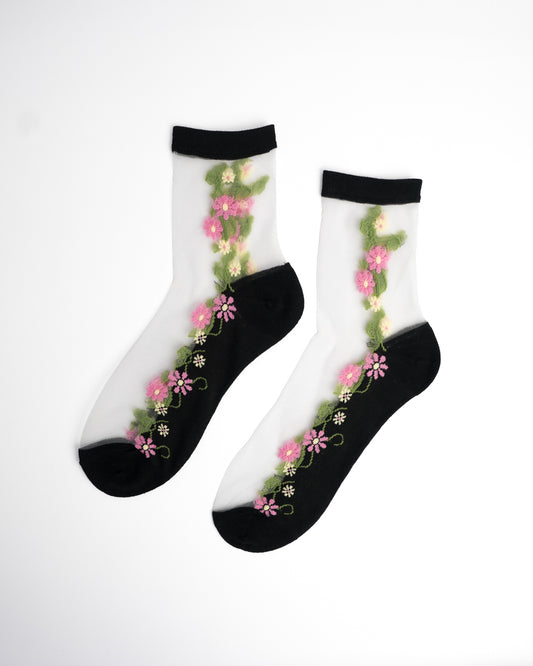 Pink Daisy Sheer Crew Socks in black with pink floral and green vine embroidery on flat lay white background