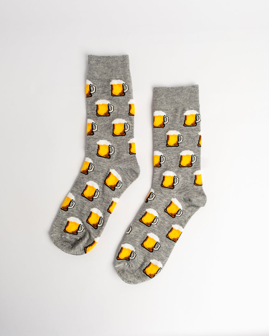 A pair of heather gray crew socks with a repeating pattern of yellow beer mugs filled with golden beer and topped with white foam, displayed on a clean white background.