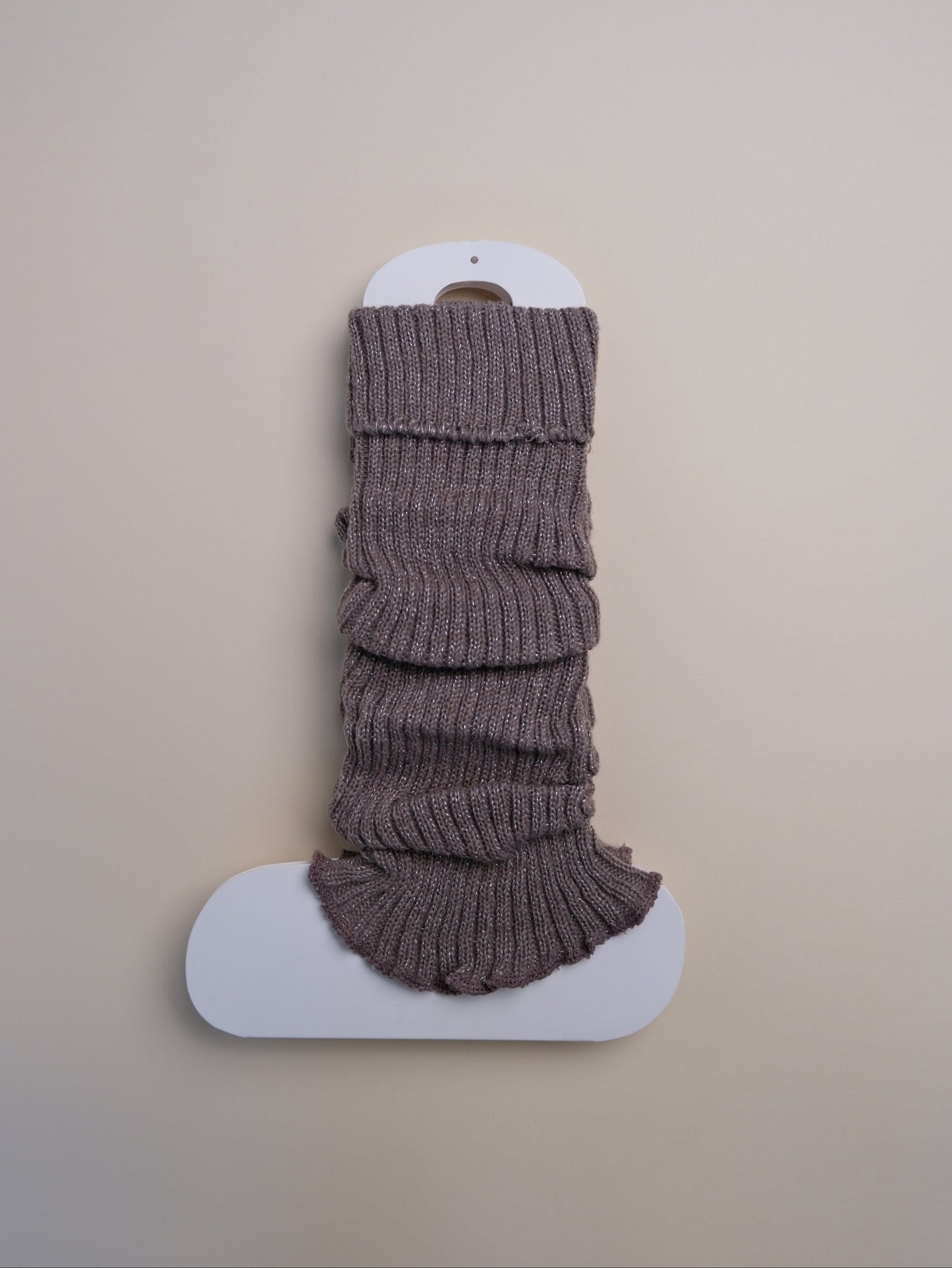 Brown ribbed leg warmers on a white stand against a beige background