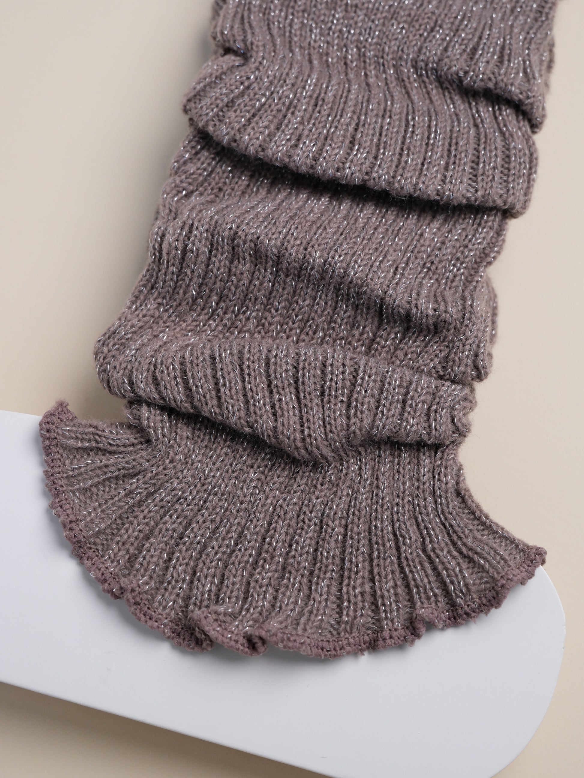 Knitted leg warmers on a white surface with a beige background