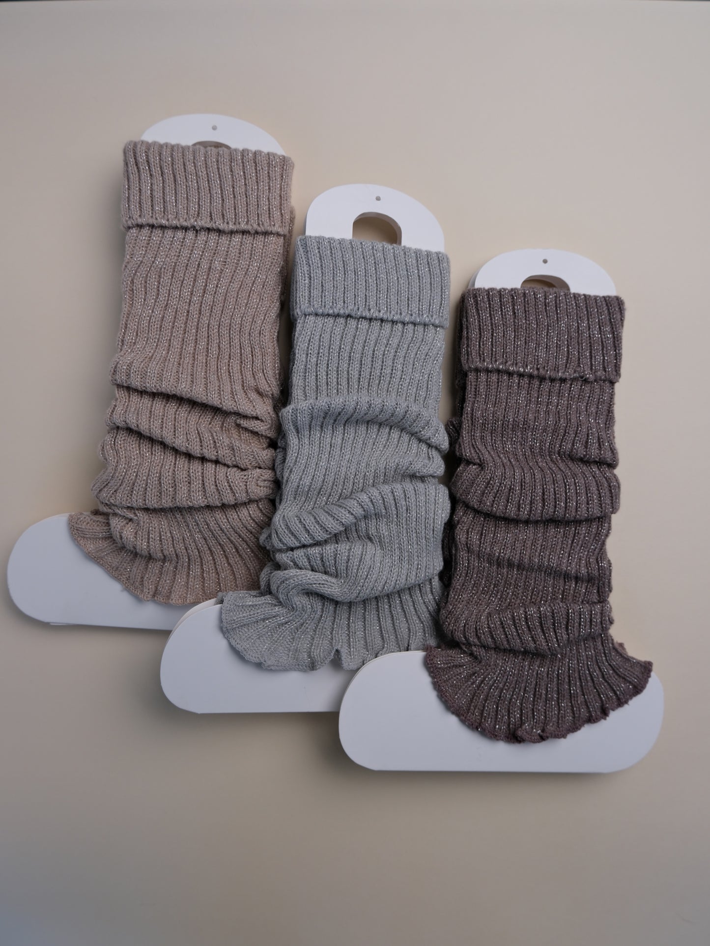 Three pairs of ribbed leg warmers in brown, gray, and brown on a beige background.