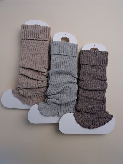 Three pairs of ribbed leg warmers in brown, gray, and brown on a beige background.