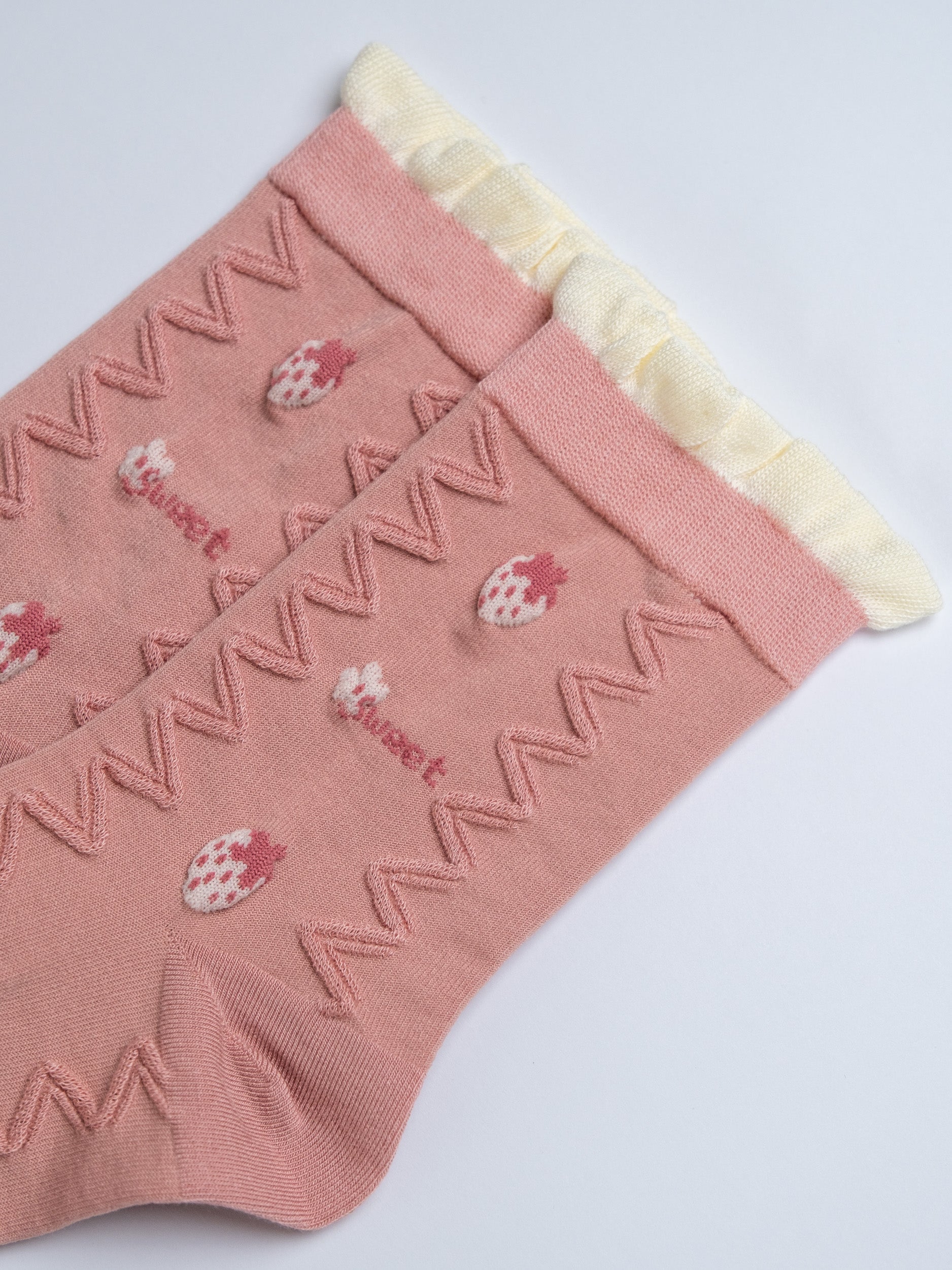 Pink socks with strawberry design and white trim on a light gray background