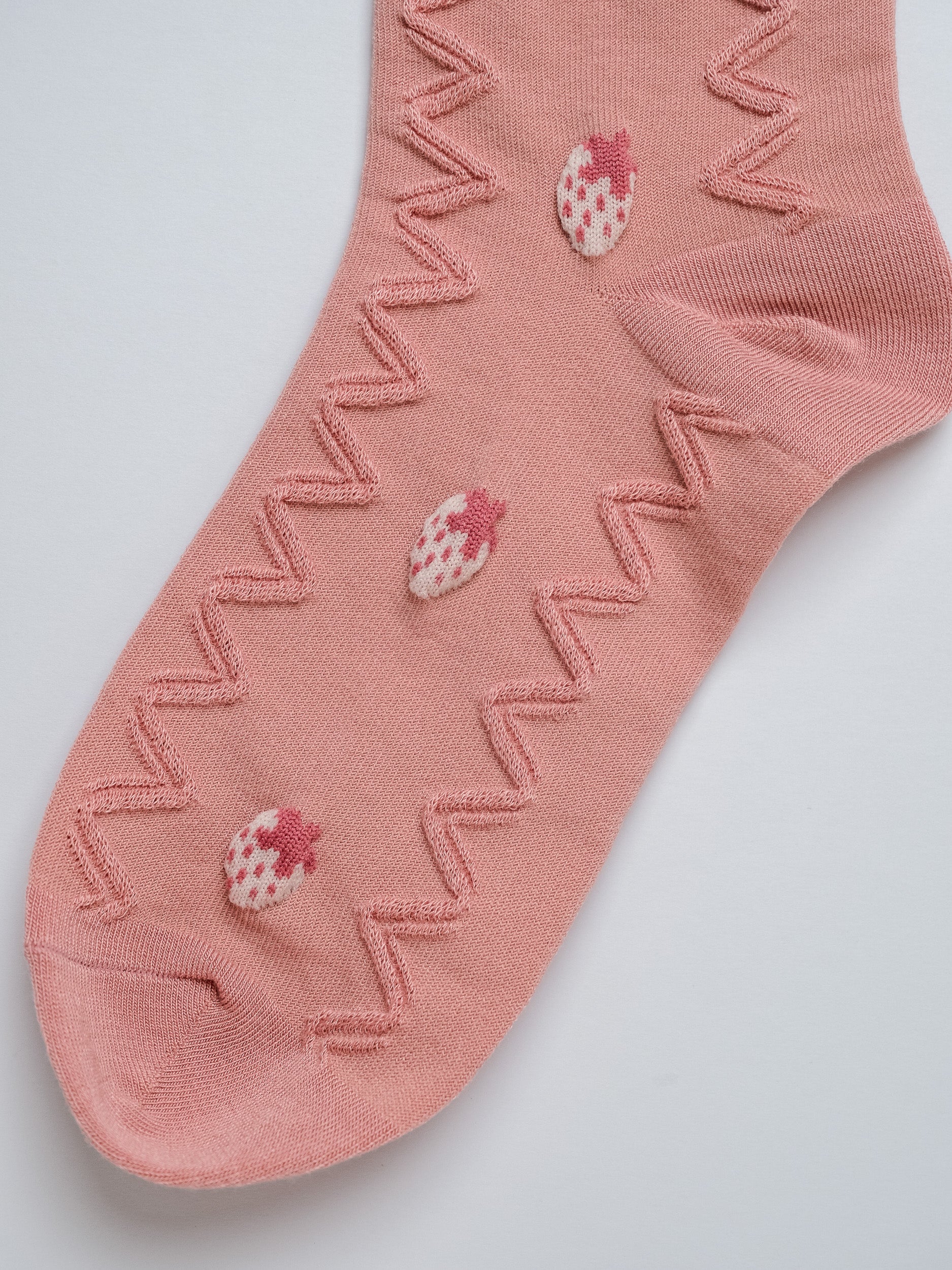 Pink sock with strawberry patterns on a light gray background