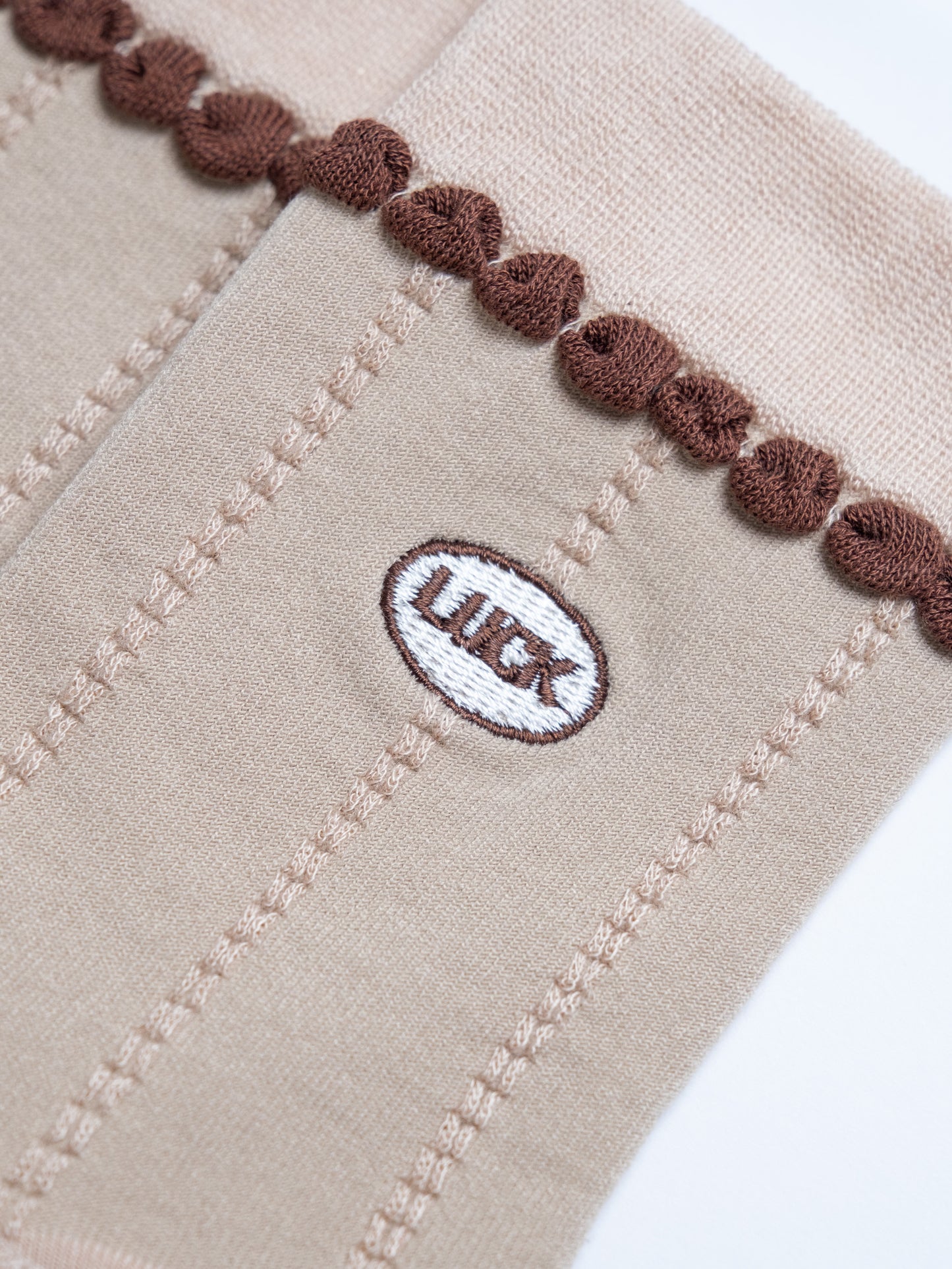 Close-up of beige fabric with brown trim and a logo on a white background